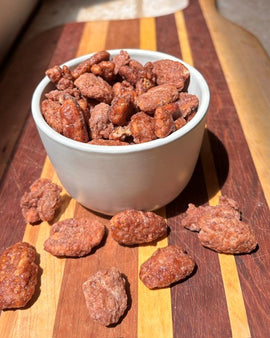 Praline crunch pecans in a rustic bowl on a wooden board with sweet crunchy praline coating